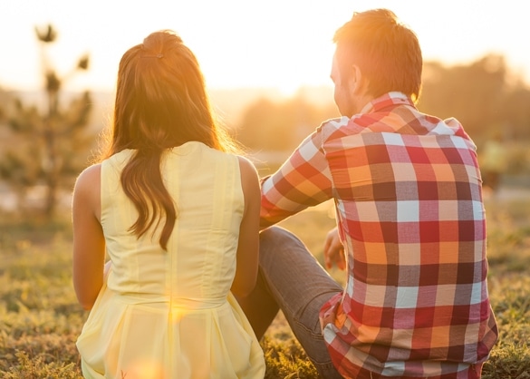 back view of young happy couple sitting on river at sunset - Pros and Cons to Dating a Gemini Man